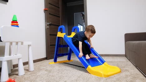 active toddler boy playing on the slide in his room. cute baby climbs up backwards.