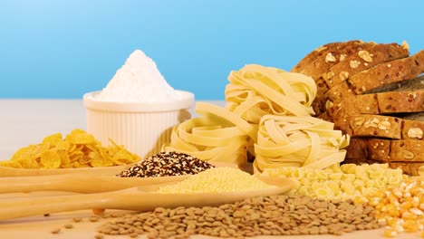 a variety of grains, pasta, and bread displayed on a wooden surface with a bright blue backdrop