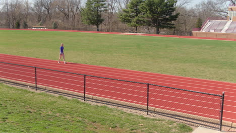 Teen-girl-warming-up-on-the-track-looks-up-towards-camera-as-she-walks-by