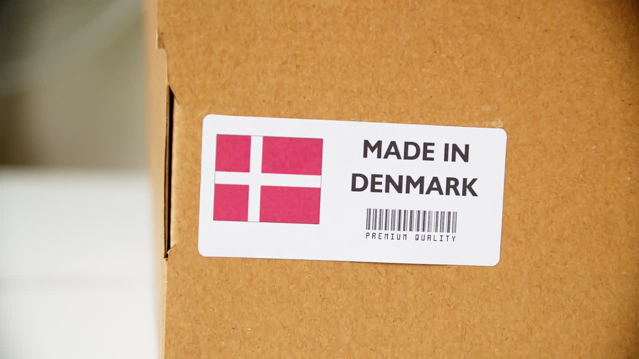 Hands applying MADE IN DENMARK flag label on a shipping cardboard box with products