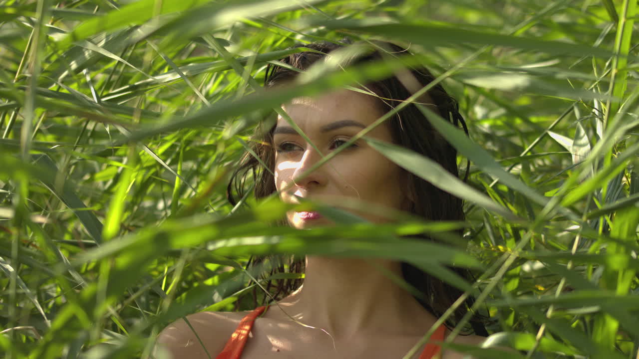 Portrait of a young woman standing amongst reeds by the lake during sunset