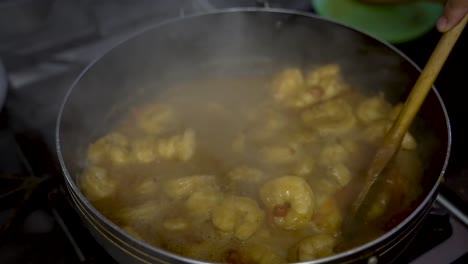 curry prawns dish stirred by a wooden ladle with cooking with steam vapour rising