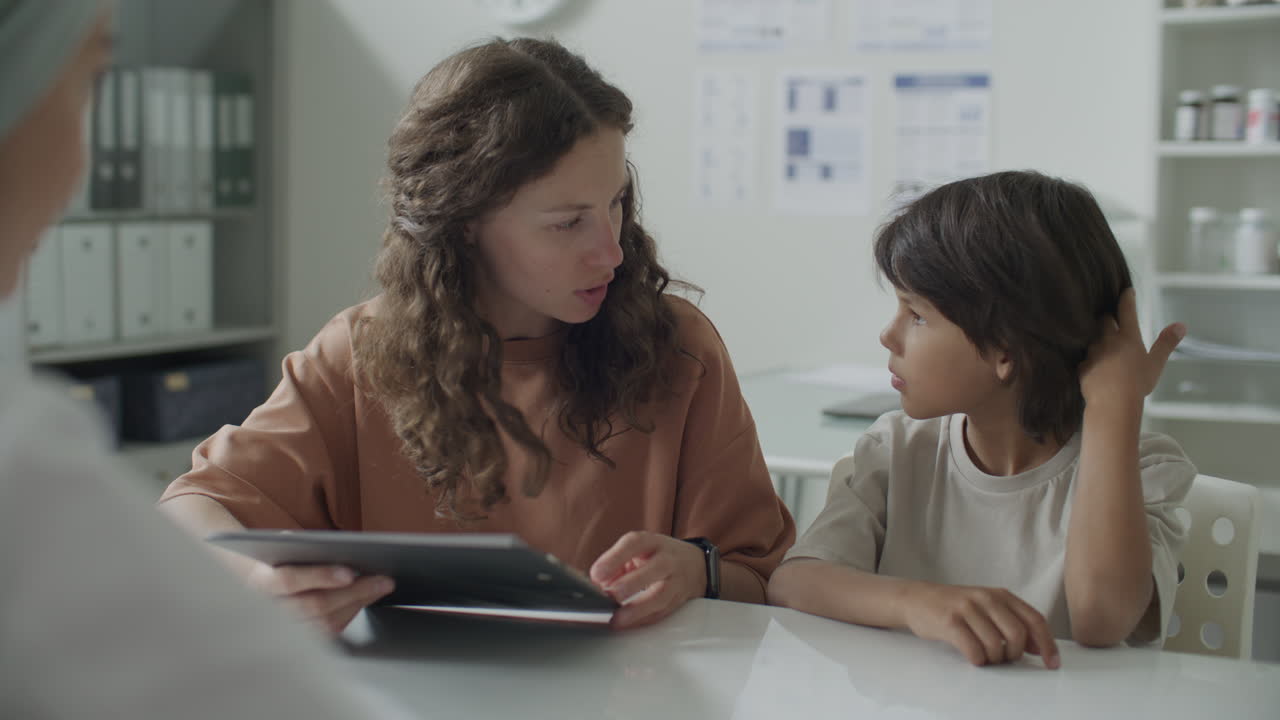 Woman with Child Reviewing Medical Documents and Speaking with Doctor in Clinic