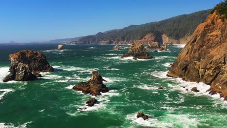 scenic aerial shot gliding over ocean waves and sea stack rock formations. shot by an evergreen forest and cliffside on the shores of oregon, pacific northwest.