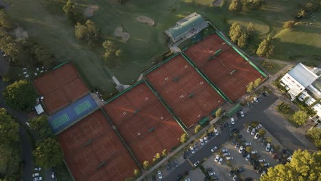 aerial rising above clay tennis courts and a professional golf course with obstacles in sport club at sunset