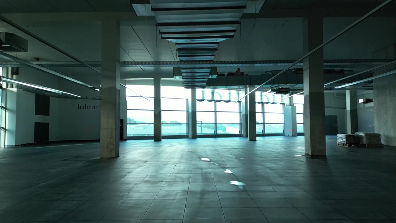 Interior espacioso y vacío de una obra en construcción con columnas de hormigón y grandes ventanales durante el día