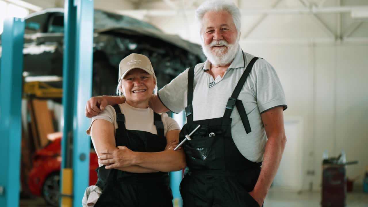 retrato de un hombre y una mujer adultos mecánicos en uniforme de pie y mirando a la cámara en el servicio de automóviles