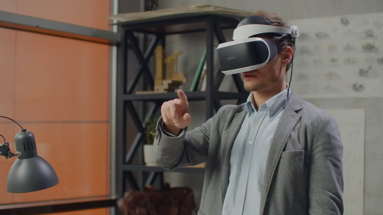 Young male engineer in office in virtual reality helmet with hands makes movements imitating the work of graphic interface.