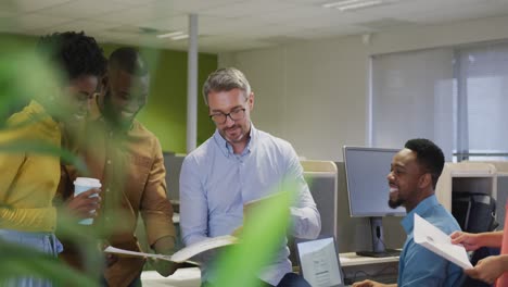 happy diverse male and female business colleagues using tablet and talking in office