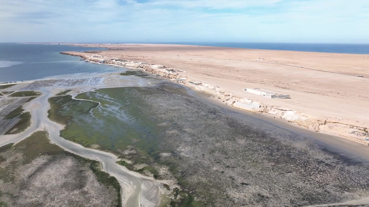 Drohnen-Luftaufnahme von Küstenfeuchtgebieten, Gezeitenkanälen und einem Strandresort entlang der Dakhla-Lagune, die die einzigartige Wechselwirkung zwischen Marokkos Atlantik-Sahara und ihren Küstenökosystemen zeigt.