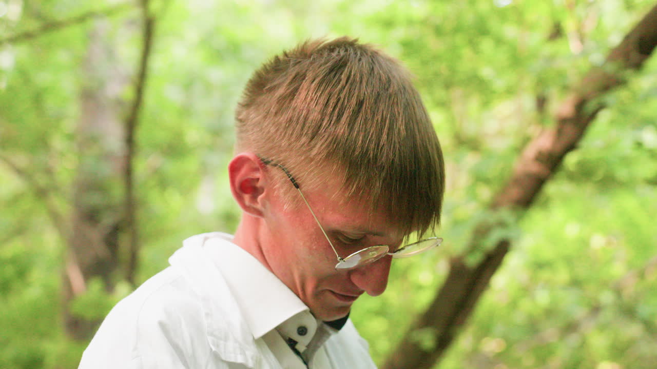 Portrait side view of ecologist in white coat standing in forest looking focused, surrounded by lush greenery and natural light, highlighting outdoor preparation, concentration, and lifestyle detail