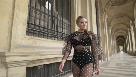 stylish woman in polka dot dress walking through parisian archway