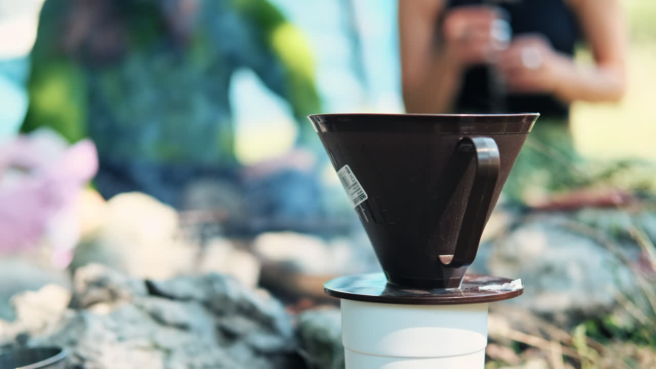 A cup with two persons dealing with the campfire on the background. Preparing coffee