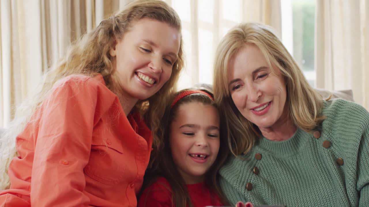 소파에 앉아서 스마트폰을 함께 보는 행복한 백인 어머니, 딸, 할머니의 비디오