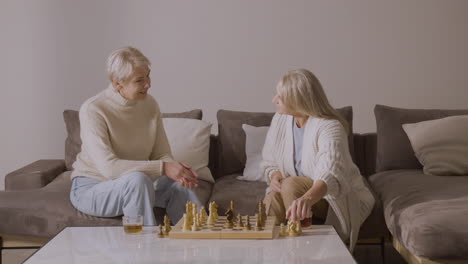 dos mujeres mayores jugando ajedrez sentadas en un sofá en casa