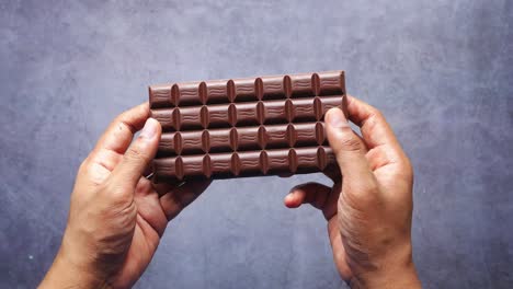 hands holding a broken and whole dark chocolate bar