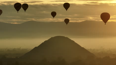 Pyramid-structure-and-Hot-air-balloons,-backlit-by-a-hazy-sunrise-sky---Aerial-view