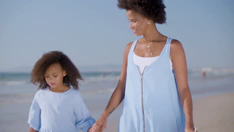 mum and daughter holding hands and walking along seashore on a sunny day