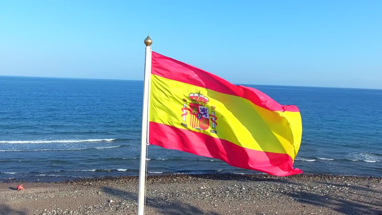 Roterende optagelse af Spaniens nationalflag på stranden.
