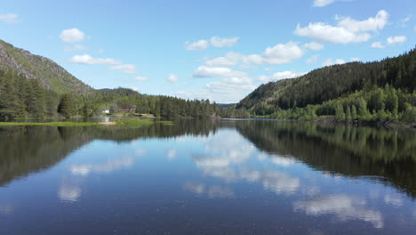 aerial view between trees, over a calm, reflecting tovdalelva river, on a sunny day, in agder,, norway - dolly, drone shot