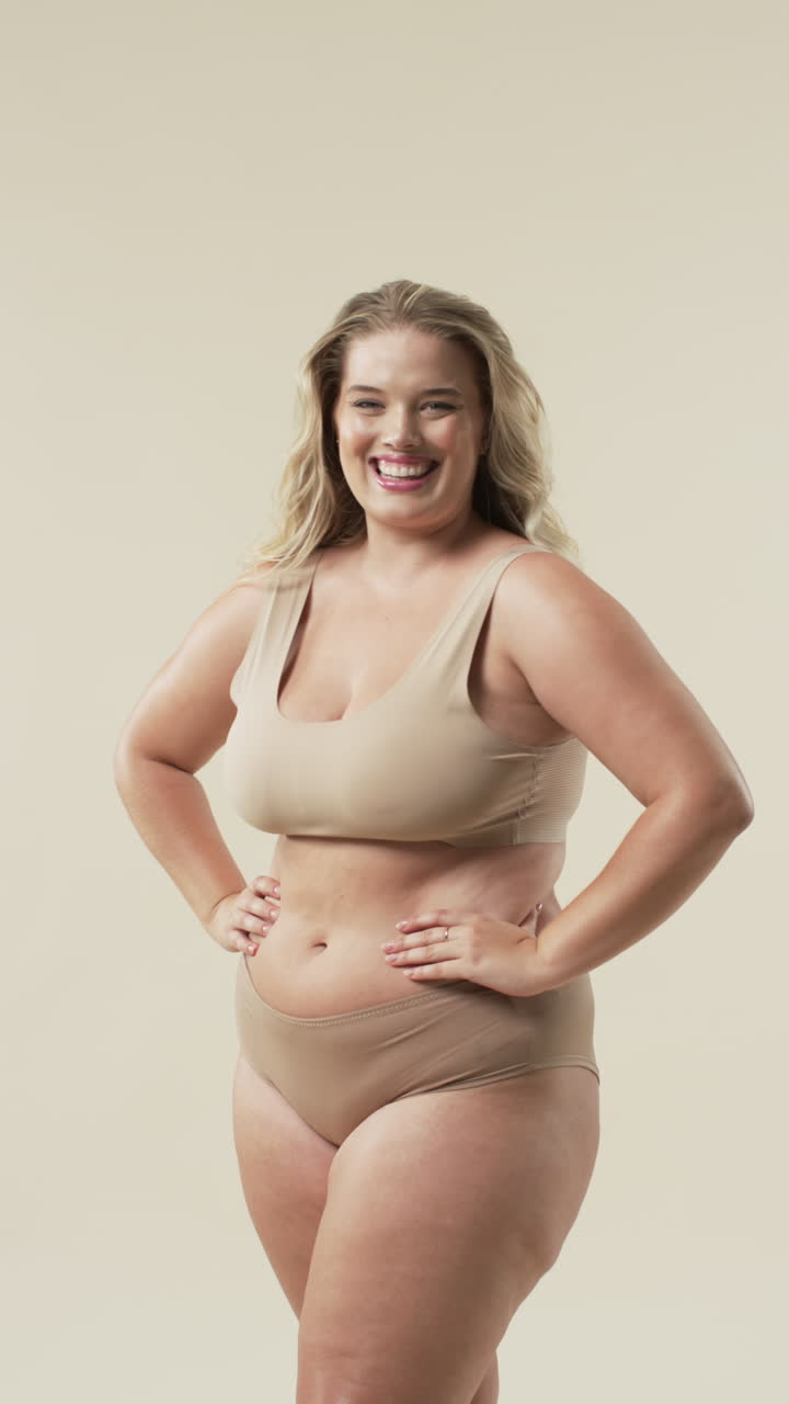 Vertical video: Confident plus size woman in beige underwear posing, embracing body positivity