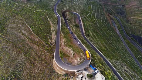 winding mountain road in lanzarote island with many cars and yellow bus, aerial view