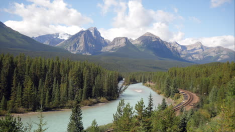 Time-lapse-of-a-turquoise-colour-river,-mountains-in-the-back,-and-train-track-in-the-front