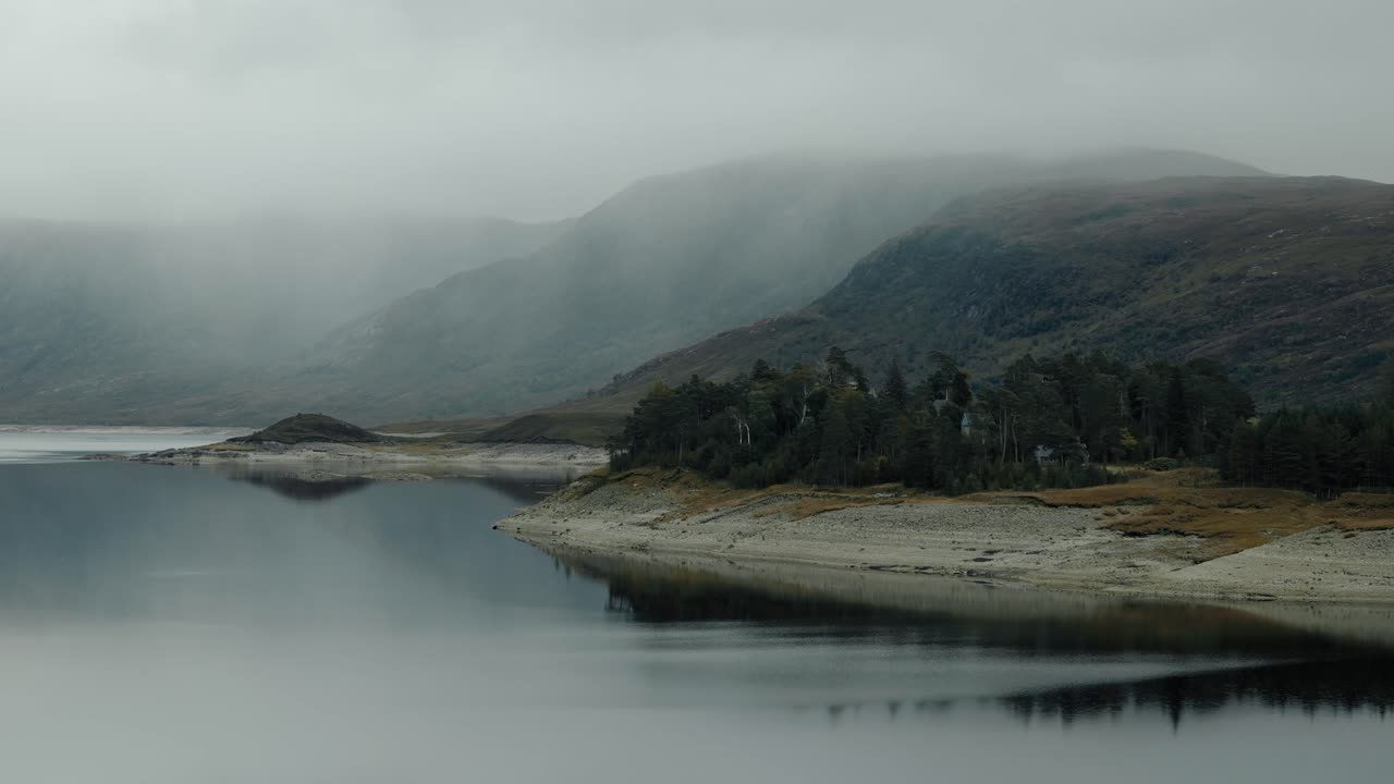 Approaching ascending shot toward a moody tree grove reflected in Loch Cluanie, Scotland