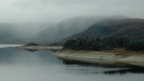 approaching ascending shot toward a moody tree grove reflected in loch cluanie, scotland
