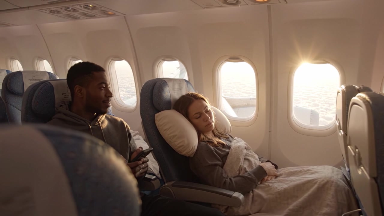 Passagiere entspannen sich in Flugzeugsitzen, während offene Fenster warmes Sonnenlicht über den Wolken reflektieren und ein ruhiges Reiseerlebnis bieten.