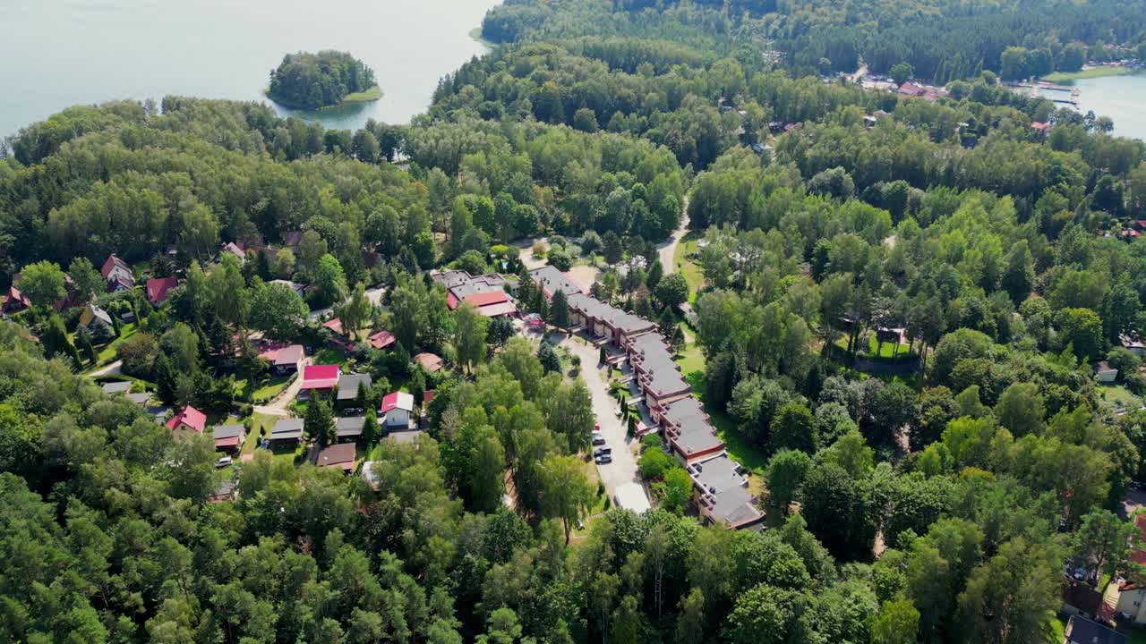 Drone view of a picturesque tourist village surrounded by trees, with the blue waters of the lake visible in the background