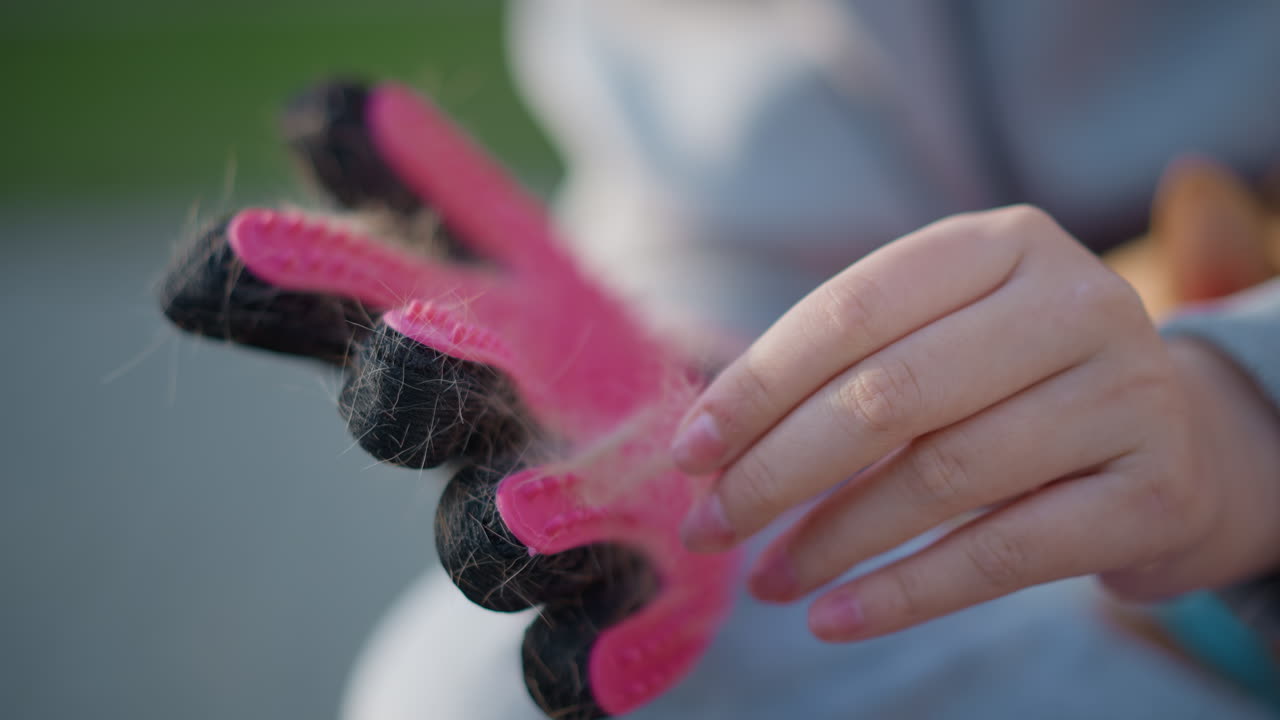 장갑 표면의 털을 조심스럽게 제거하는 사람, 부드러운 동작으로 장갑에서 보풀을 털어내는 손의 클로즈업, 부드러운 햇빛 아래에서 장갑의 털과 보풀을 제거하는 손을 보여주는 디테일 이미지