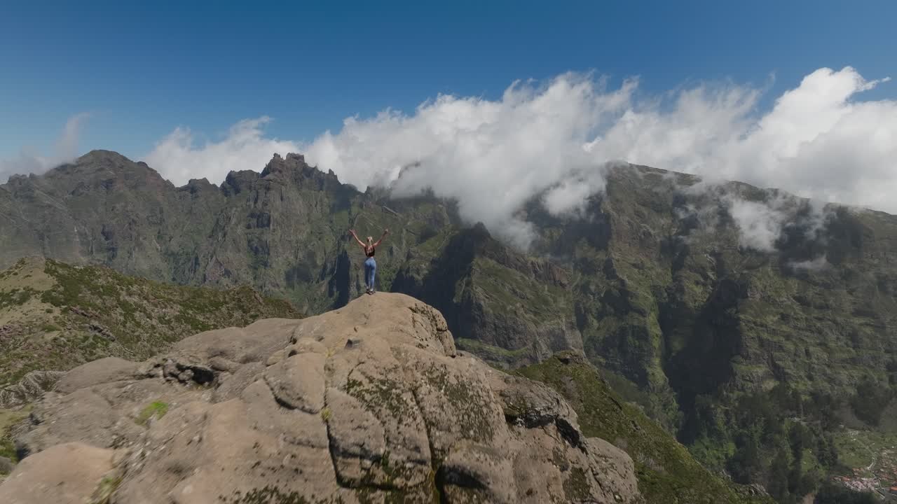 mujer atlética camina a la cima de la montaña en un día soleado levantando los brazos en el aire