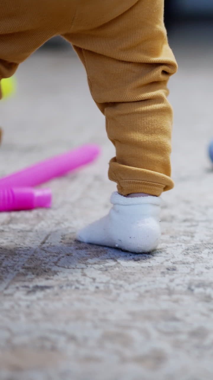 Little feet of a baby in white socks. Active baby boy runs by the carpet with scattered toys. Vertical video