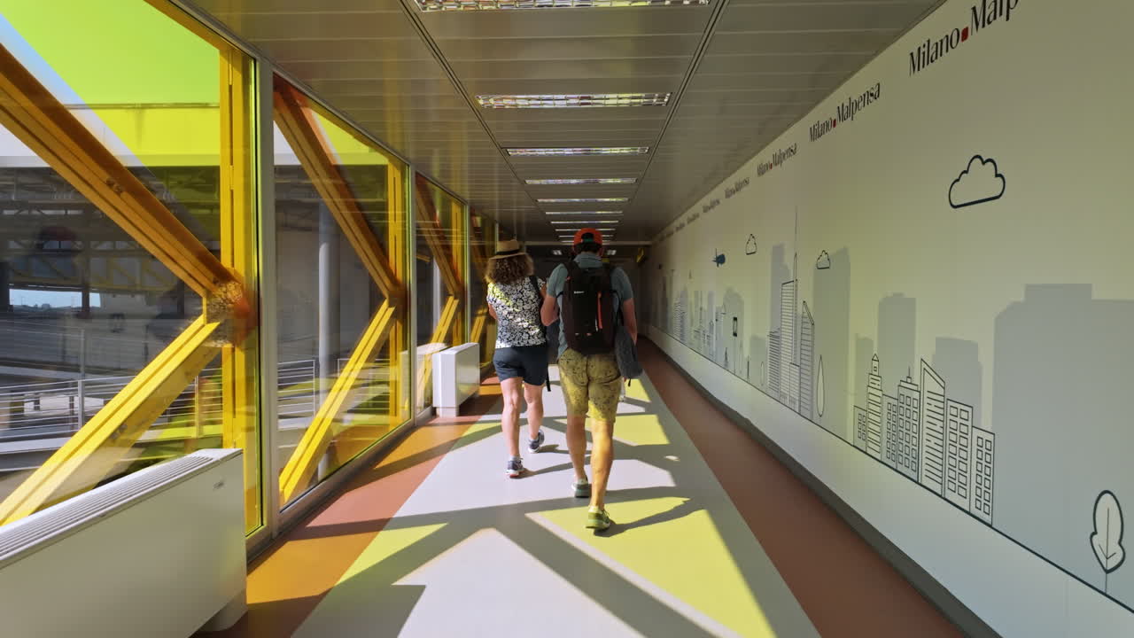Two travelers walking through a colorful, sunlit airport hallway with bright yellow accents