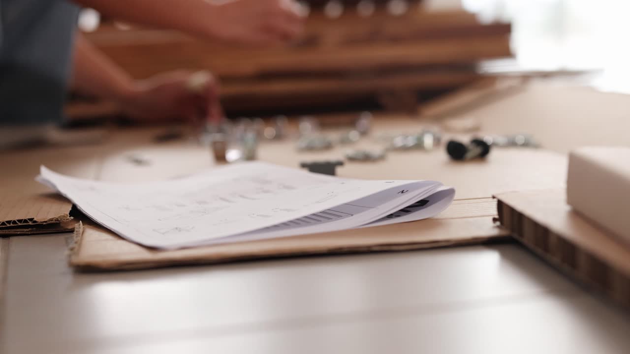 Hands assembling furniture using instructions and tools on a table. Bright lighting and focused actions create a productive atmosphere