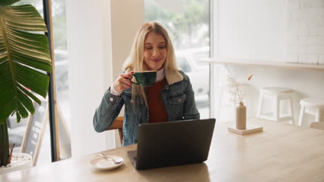 woman drinking coffee at a cafe while working on a laptop