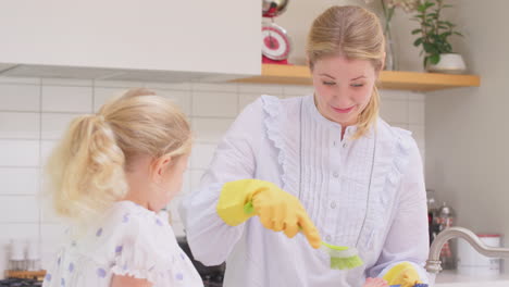 Madre-Usando-Guantes-De-Goma-En-Casa-En-La-Cocina-Con-Su-Hija-Pequeña-Divirtiéndose-Mientras-La-Niña-Pone-Los-Pies-En-El-Fregadero-Mientras-Ellos-Lavan-En-El-Fregadero,-Filmada-En-Cámara-Lenta