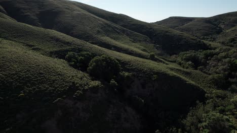 drone push in tilt up along dark shadowy subdued green rolling hillside
