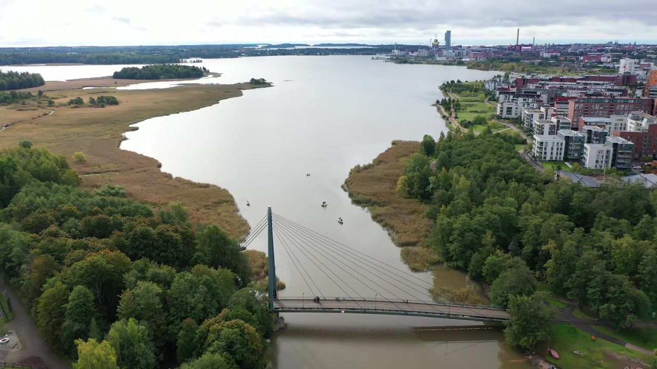 Ampia ripresa aerea dello skyline urbano di Helsinki con i grattacieli di Kalasatama e la centrale elettrica di Hanasaari attraverso la baia di Vanhankaupunginselkä. Paesaggio costiero scenografico sotto un cielo cupo e nuvoloso
