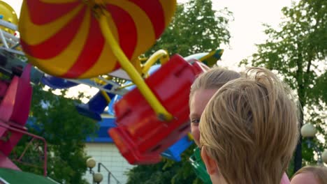 close-up of the face of a mother with her son standing near a fast spinning carousel, the wind from the carousel develops the blonde hair of a woman and a child. have fun at the sunday fair