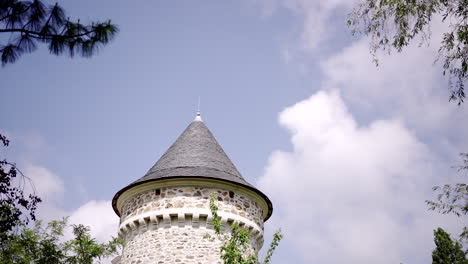 Stone-castle-tower-with-conical-roof-against-a-bright-blue-sky-and-greenery