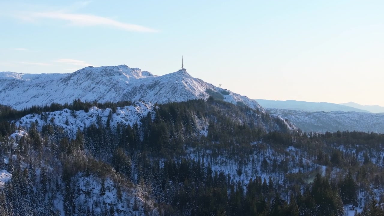 Volo di drone sopra foreste innevate sul Monte Fløyen con il Monte Ulriken in lontananza.