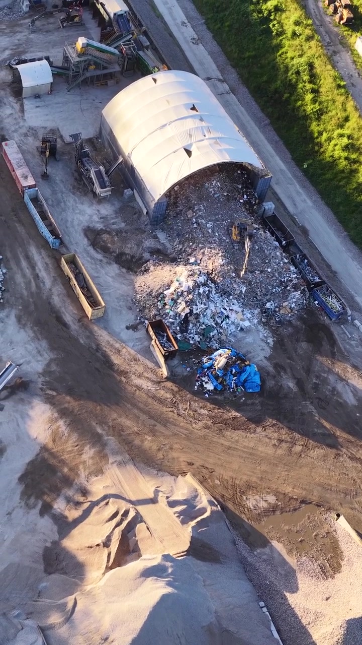 Una ripresa aerea con drone cattura macchinari pesanti e cumuli di rifiuti in un centro di riciclaggio industriale.