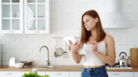 the girl in the white kitchen holds a tablet in her hands and considers the diet