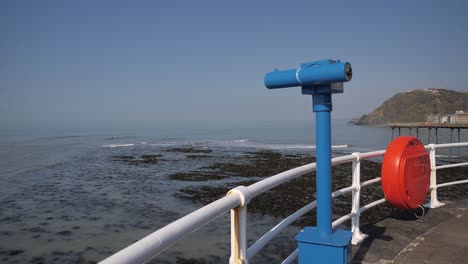 a sea viewing telescope points out to the irish sea on the promenade, aberystwyth, ceredigion, wales on a beautiful clear day. also on view in the shot is a plastic cover for a life saver ring.