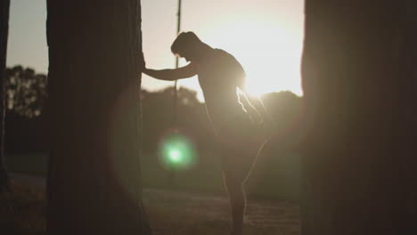 man in park stretches out legs before going for a run whilst being silhouetted by the sun