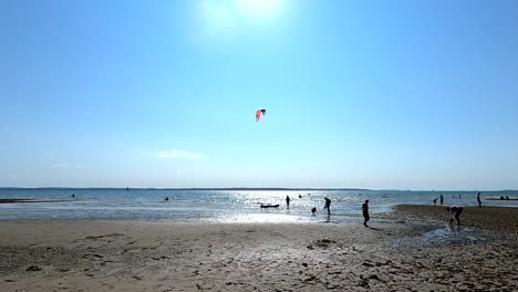 Una-Escena-De-Playa-En-Verano-Con-Gente-Caminando-Y-Kitesurfistas-En-El-Agua