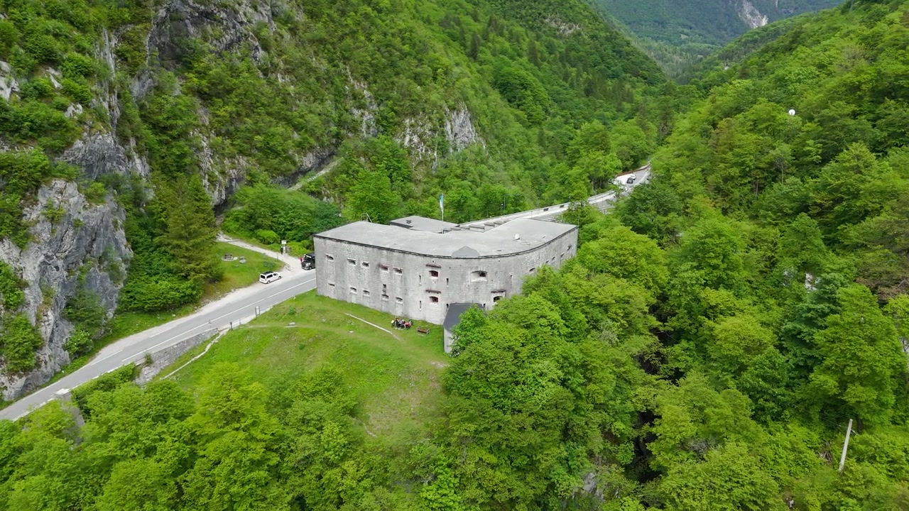 En historisk fæstning omgivet af frodige skove og dramatiske bjerge, der viser den tidløse skønhed ved Fort Kluže nær Bovec i Soča-dalen, Slovenien - Orbit droneoptagelse.