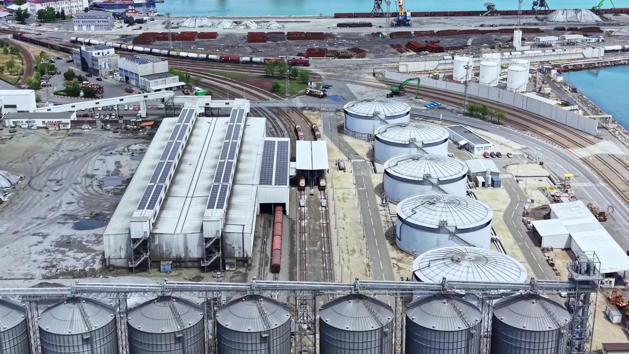 Industriegebiet mit Lagertanks und Gleisen an einer Uferpromenade in einer Küstenstadt, tagsüber.